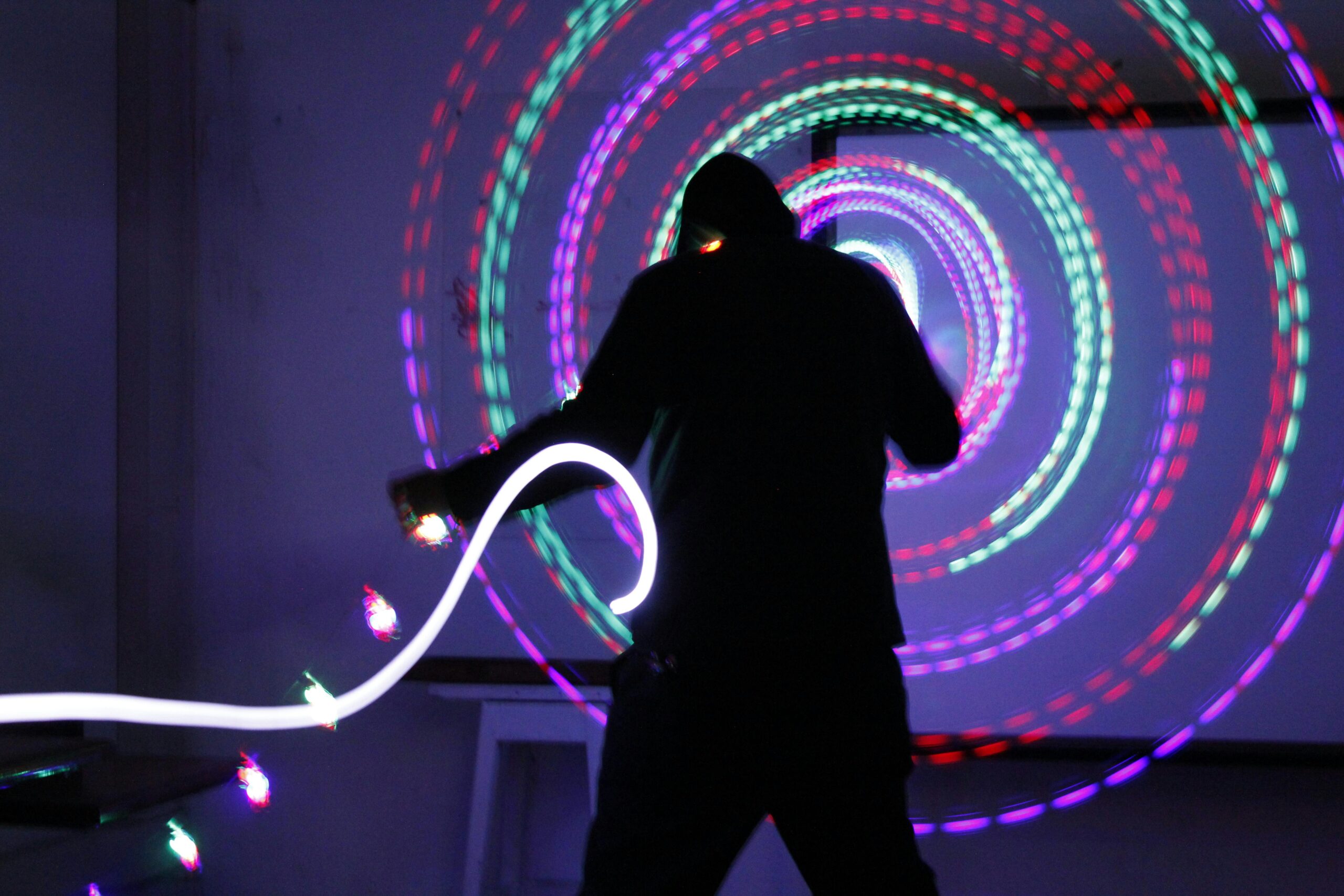 Silhouette of a performer spinning colorful LED poi in a dark room with a dazzling light trail effect.